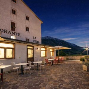 Terrazza panoramica hotel Opi La Pieja al tramonto con ristorante illuminato, tavoli esterni e vista sulle montagne