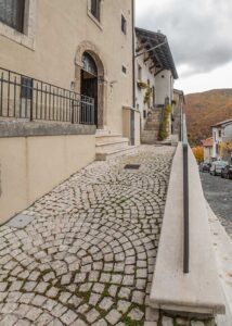 Accesso a dimora storica Opi con ingresso rialzato, pavimentazione in pietra e scorcio del borgo tra le montagne