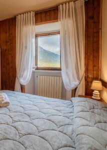 Camera accogliente dimora storica Opi con letto matrimoniale, dettagli in legno e finestra con vista sulle montagne