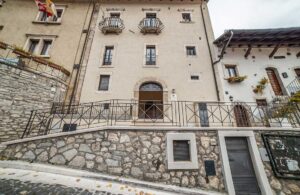 Facciata esterna dimora storica Opi con portale in pietra, balconi in ferro e architettura autentica del borgo