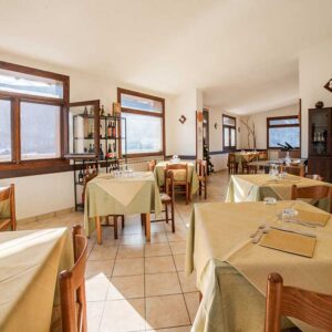 Sala interna ristorante Opi con tavoli apparecchiati, luce naturale e ambiente accogliente di montagna